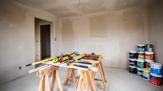 Intérieur de maison en chantier avec murs en placo brut et outils de finition posés sur des tréteaux