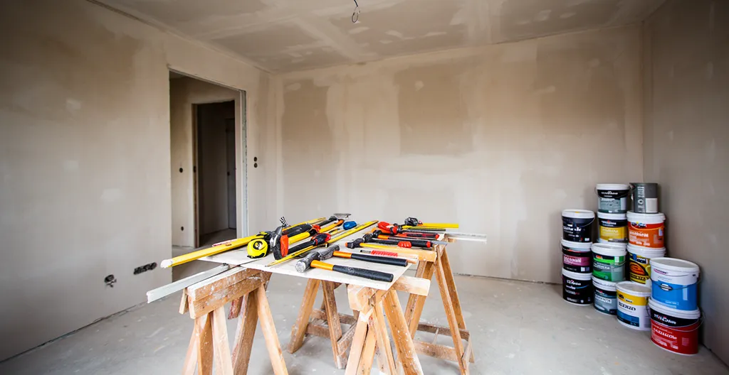 Intérieur de maison en chantier avec murs en placo brut et outils de finition posés sur des tréteaux